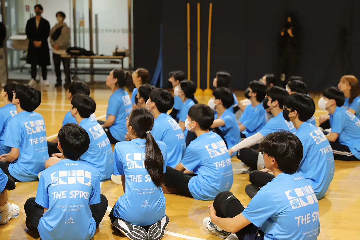Participants wearing The Spike T-shirts seated together on a gym floor